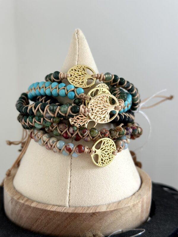 Stapel van "Beach Serenity's" armbanden van Little Caribbean, met kleurrijke turquoise, groene en aardse kralen en gouden levensboom bedels, op een decoratieve standaard.