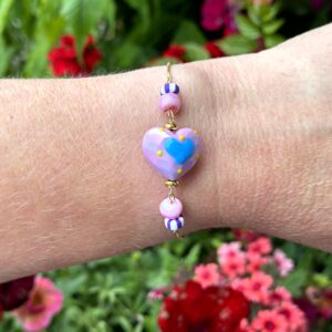 "Sea Hearts" armbandje van Little Caribbean met een hartvormig middelpunt en kleurrijke kralen, gedragen op een pols.