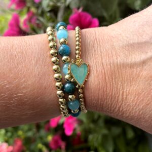 "Tropical Bliss" armbandenset van Little Caribbean met gouden kralen en een blauw hartvormig hangertje, gedragen op een pols.