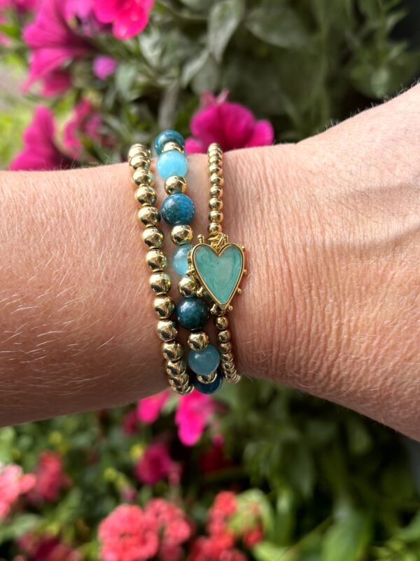 "Tropical Bliss" armbandenset van Little Caribbean met gouden kralen en een blauw hartvormig hangertje, gedragen op een pols.