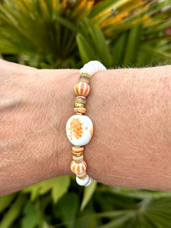 "Tropical Paradise" armband van Little Caribbean met witte, gouden en oranje kralen, gedragen door een arm met een groene achtergrond.